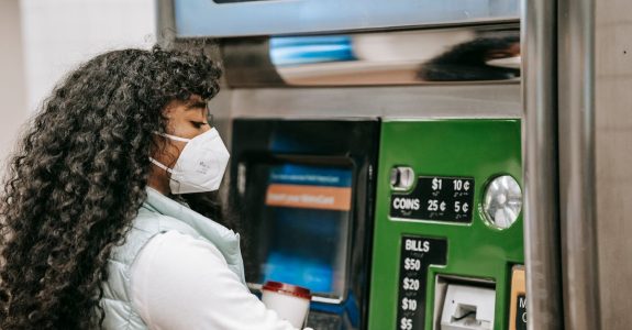 a-woman-wearing-a-face-mask-uses-a-ticket-machine-for-purchasing-fare-in-a-public-setting-reflectin-1